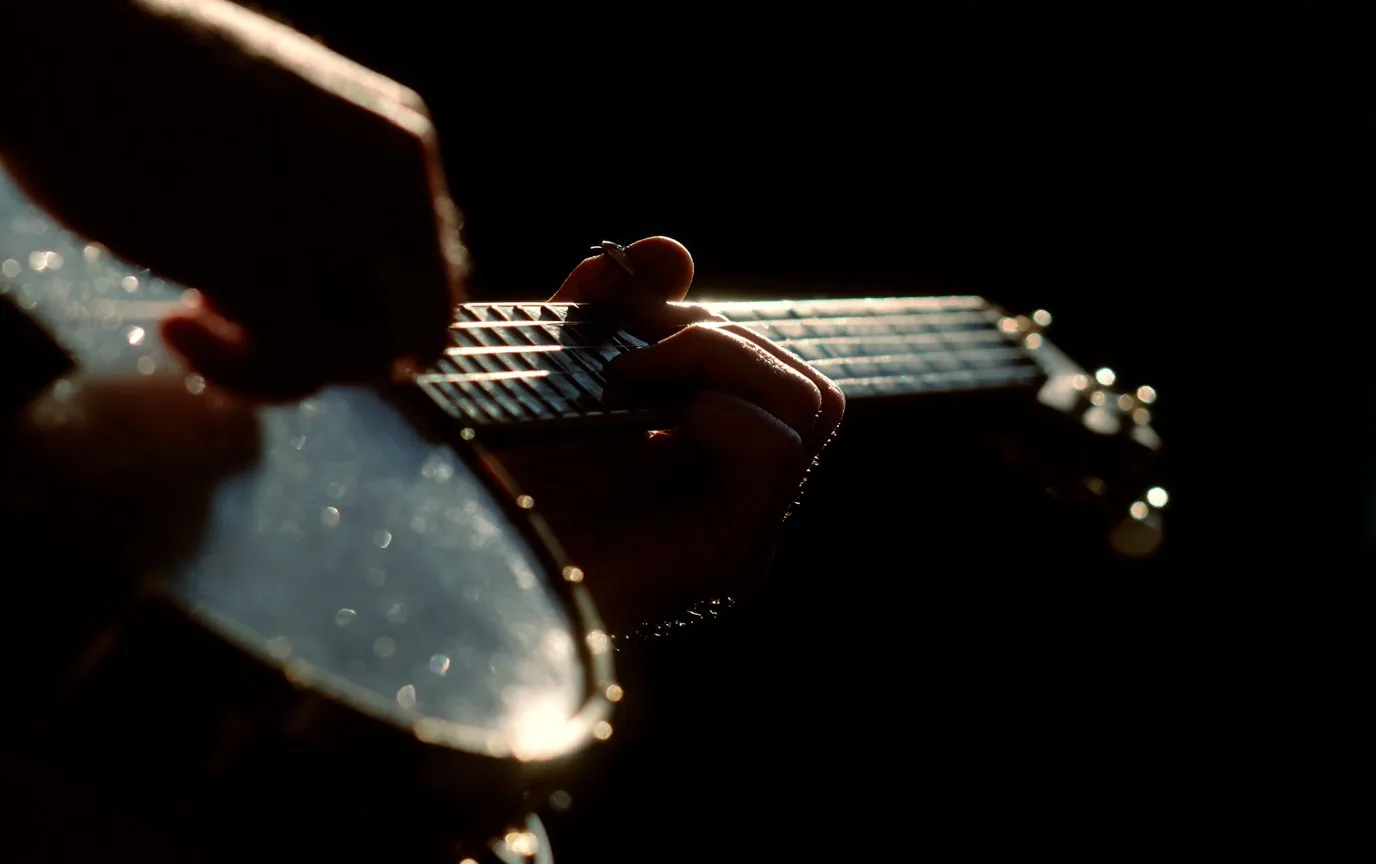 A hand turning a tuning peg on a tenor banjo headstock
